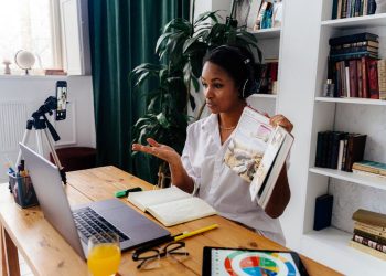 Woman conducting online teaching session at home with laptop and books.